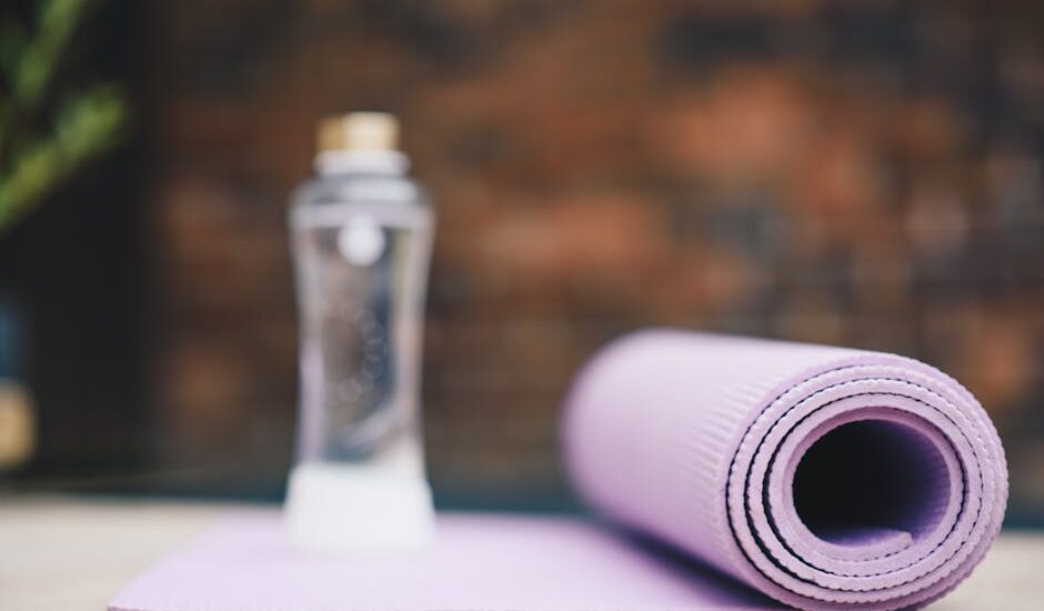 A rolled purple fitness mat and a clear spray bottle, illustrating cleaning tips for maintaining a germ-free workout space