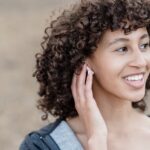 Young woman smiling while adjusting her hearing aid, illustrating the process of handling hearing aids for battery replacement.