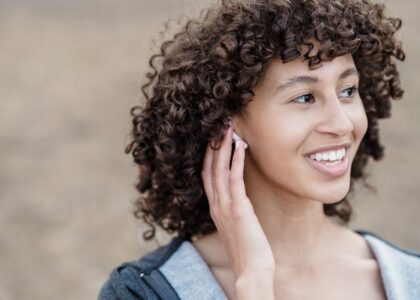 Young woman smiling while adjusting her hearing aid, illustrating the process of handling hearing aids for battery replacement.