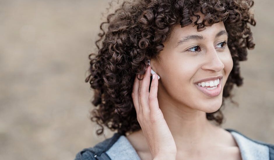 Young woman smiling while adjusting her hearing aid, illustrating the process of handling hearing aids for battery replacement.