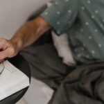 Person in bed reaching for eyeglasses on a bedside table, illustrating a relaxed morning routine while weaning off CPAP therapy.