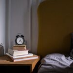 A cozy bedroom setting with books and an alarm clock on a nightstand next to a bed.