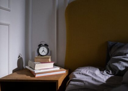 A cozy bedroom setting with books and an alarm clock on a nightstand next to a bed.