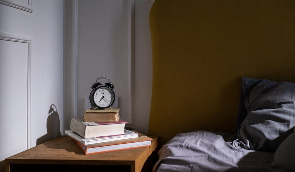 A cozy bedroom setting with books and an alarm clock on a nightstand next to a bed.