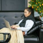 Person relaxing on a black sofa with an infrared heating pad draped over their shoulders, working on a laptop, for an article about infrared heating pads worth