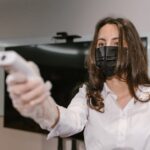 Woman wearing face mask using an infrared thermometer indoors.