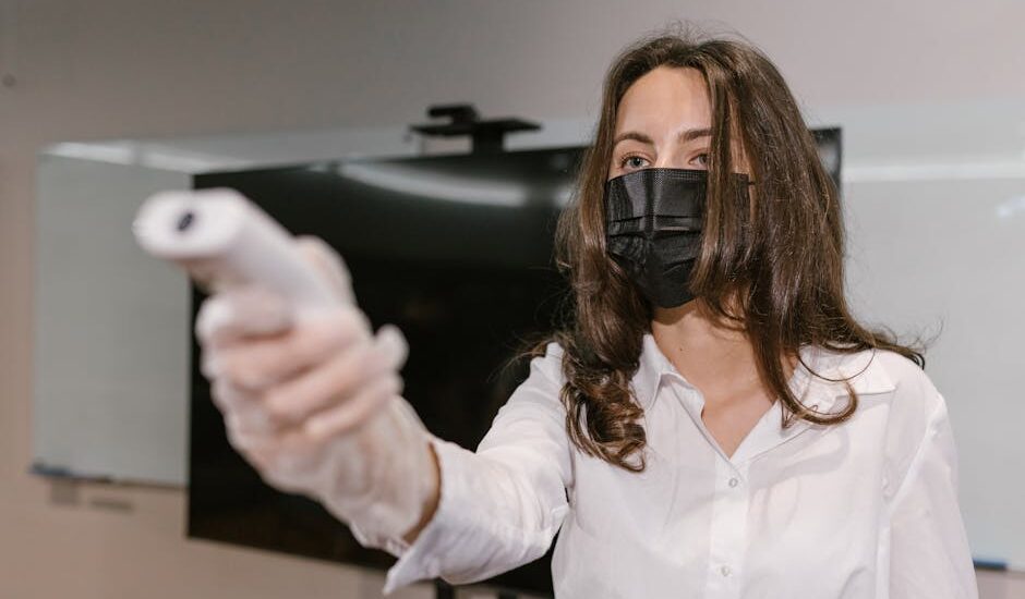 Woman wearing face mask using an infrared thermometer indoors.