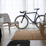 A standard bicycle stands between two chairs and a coffee table in a bright home office, illustrating workspace fitness ideas for desk cycle discussions.