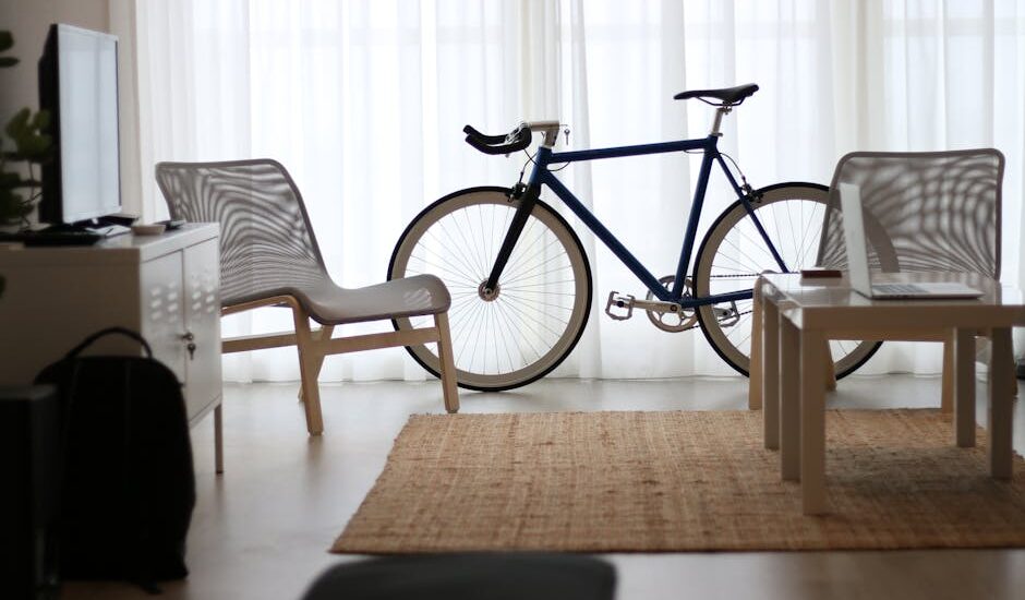 A standard bicycle stands between two chairs and a coffee table in a bright home office, illustrating workspace fitness ideas for desk cycle discussions.