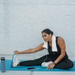 A woman stretches on a yoga mat with a towel, phone, and a smart water bottle nearby, illustrating hydration tech use.