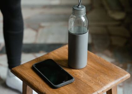 Close-up of a smartphone and water bottle placed on a wooden stool inside a room.
