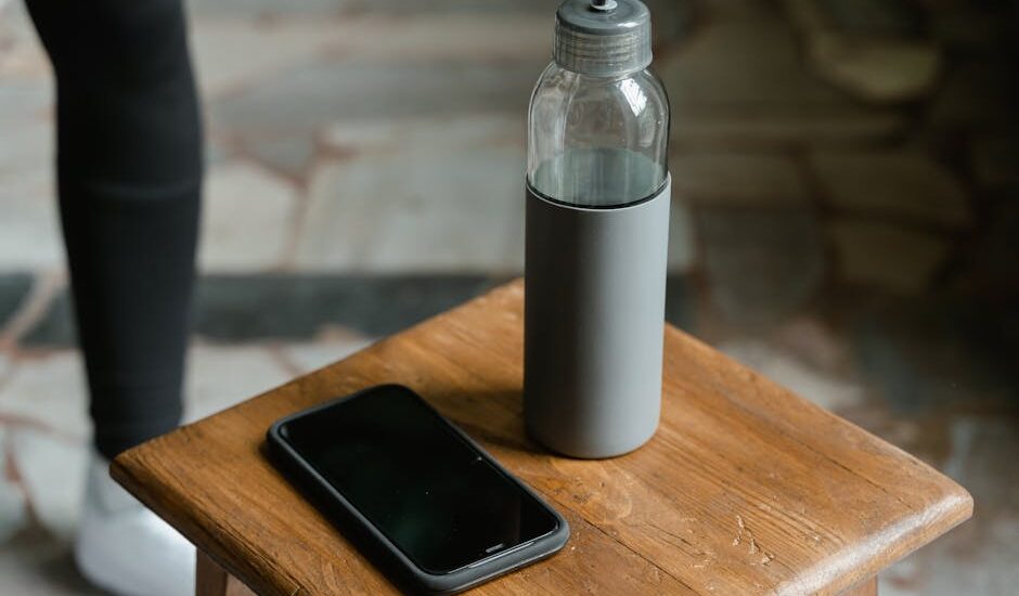 Close-up of a smartphone and water bottle placed on a wooden stool inside a room.