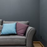 Part of soft modern gray sofa with armrest and abundance of bright pillows placed near wall in light room at home
