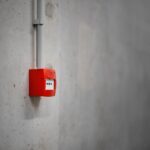A red alarm box mounted on a gray concrete wall, offering urban security.
