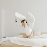 A child lifts two large white pillows on a bed, illustrating the comfort and choices discussed in orthopedic vs memory foam pillow comparisons.