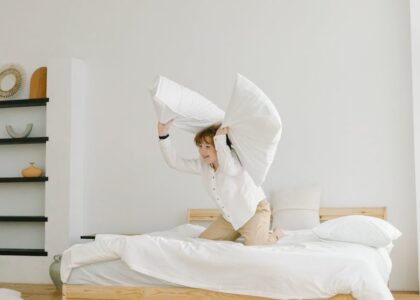 A child lifts two large white pillows on a bed, illustrating the comfort and choices discussed in orthopedic vs memory foam pillow comparisons.