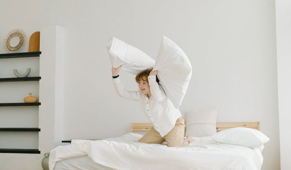 A child lifts two large white pillows on a bed, illustrating the comfort and choices discussed in orthopedic vs memory foam pillow comparisons.