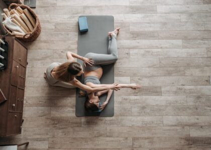 Overhead view of a yoga instructor helping a woman stretch on a mat during an indoor session.