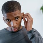 Young man adjusts a small ear device, illustrating the choice between personal sound amplifiers and hearing aids.
