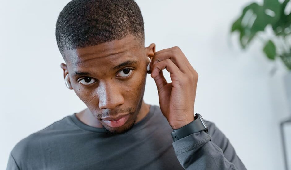 Young man adjusts a small ear device, illustrating the choice between personal sound amplifiers and hearing aids.