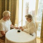 A senior couple checks their health with a finger pulse oximeter at a table in a warmly lit room.