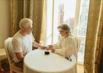 Two older adults sit at a round table in a sunlit room, using a fingertip pulse oximeter, illustrating FDA-approved device use.