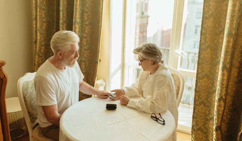 A senior couple checks their health with a finger pulse oximeter at a table in a warmly lit room.