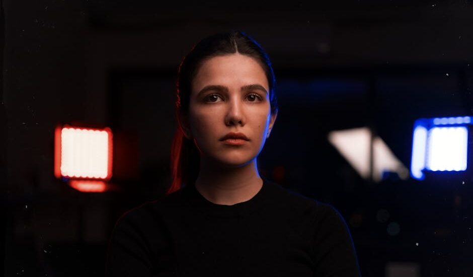 A woman sits indoors between illuminated red and blue light therapy panels, illustrating home use of red light therapy devices.