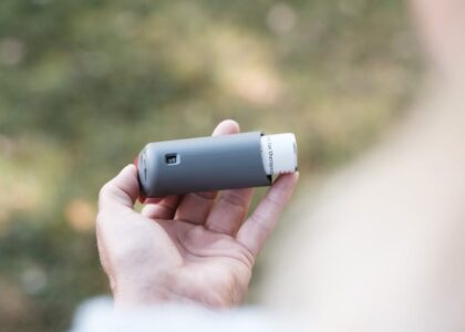 smart inhalers for asthma — Close-up of a hand holding a grey inhaler in a natural outdoor setting.