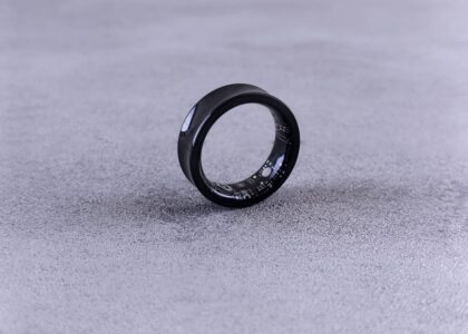 A modern black smart ring with visible circuitry resting on a textured concrete surface.