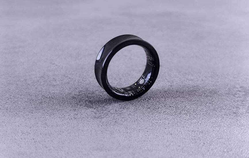A modern black smart ring with visible circuitry resting on a textured concrete surface.
