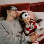 A father and daughter wearing sleep masks relax on a cozy bed, enjoying a moment together.