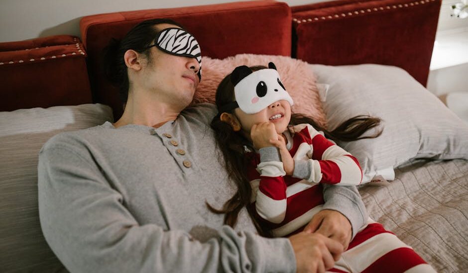 A father and daughter wearing sleep masks relax on a cozy bed, enjoying a moment together.