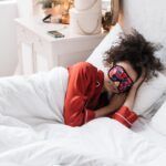 Person wearing a colorful sleep mask and red pajamas lying in bed, illustrating smart sleep mask use for better rest.