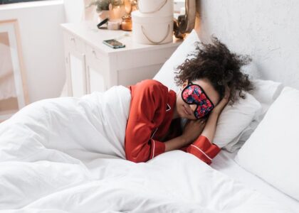 Person wearing a colorful sleep mask and red pajamas lying in bed, illustrating smart sleep mask use for better rest.