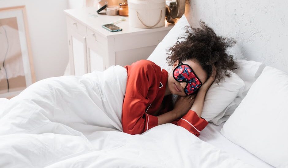Person wearing a colorful sleep mask and red pajamas lying in bed, illustrating smart sleep mask use for better rest.