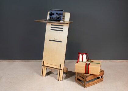 A modern wooden standing desk with a laptop and gift boxes on a crate, perfect for a minimalist office setup.