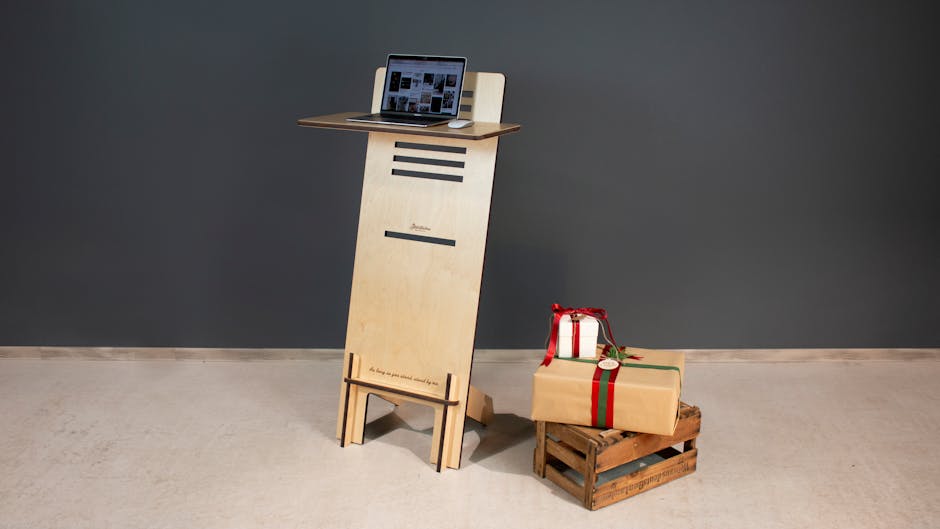 A modern wooden standing desk with a laptop and gift boxes on a crate, perfect for a minimalist office setup.