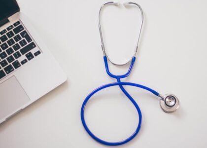 A blue stethoscope and a laptop on a white desk, illustrating the integration of digital stethoscopes in modern healthcare.