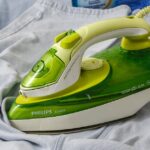 top electric heating pads — Green Philips EcoCare iron on a wrinkled shirt, ready for ironing.
