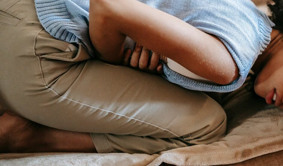 Person curled up on a couch using an electric heating pad on their abdomen, illustrating pain relief methods discussed in the article