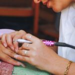 Close-up image of a nail technician using an electric file on a client's nails during a manicure session.