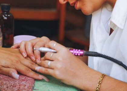 Close-up image of a nail technician using an electric file on a client's nails during a manicure session.