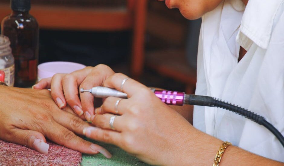Close-up image of a nail technician using an electric file on a client's nails during a manicure session.