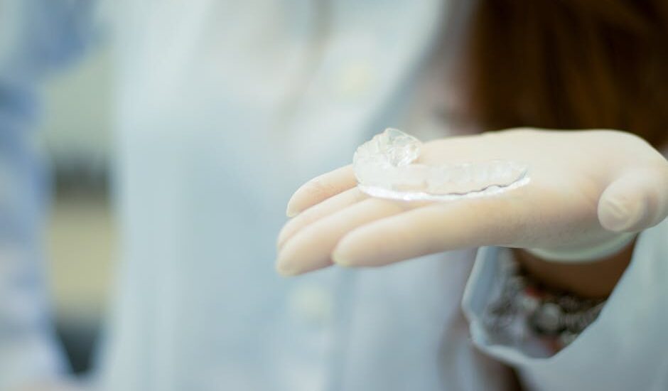 A dental professional wearing gloves holds a clear mouth guard, illustrating options for teeth grinding protection.