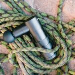 A massage gun laying on a coiled climbing rope on a rocky surface, showcasing fitness and adventure tools.