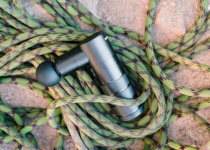 A massage gun laying on a coiled climbing rope on a rocky surface, showcasing fitness and adventure tools.