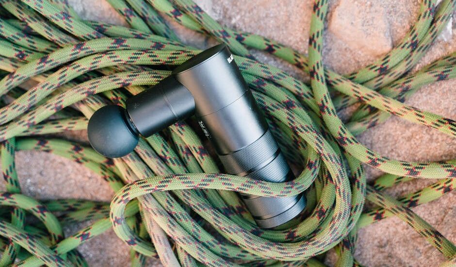 A massage gun laying on a coiled climbing rope on a rocky surface, showcasing fitness and adventure tools.