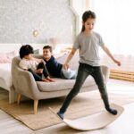 Three kids enjoying a balance board activity in a cozy bedroom setting.
