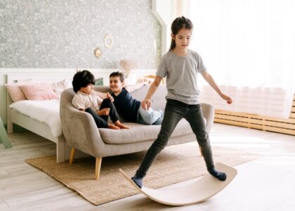 Three kids enjoying a balance board activity in a cozy bedroom setting.